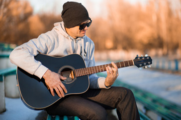 Obraz premium Young man sitting on steps playing guitar and singing