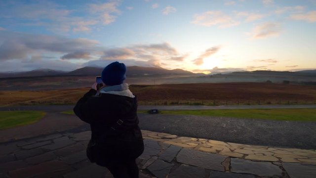 A woman taking photos of the sunset at the highland mountains in Scotland.