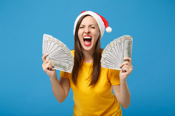 Crazy young woman Santa girl in Christmas hat posing isolated on blue background. New Year 2020 celebration holiday concept. Mock up copy space. Hold fan of cash money in dollar banknotes, screaming.