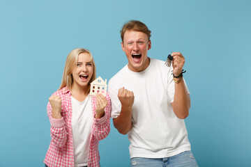 Overjoyed couple two friends guy girl in white pink t-shirts posing isolated on pastel blue background. People lifestyle concept. Mock up copy space. Holding house bunch of keys, doing winner gesture.