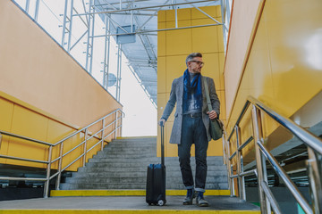 Fototapeta na wymiar Stylish gentleman holding travel suitcase and standing on stairs