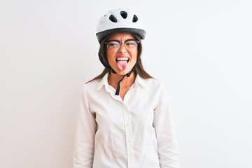 Beautiful businesswoman wearing glasses and bike helmet over isolated white background sticking tongue out happy with funny expression. Emotion concept.
