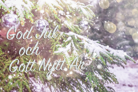 Text in Swedish "God jul och gott nytt ar"means "Merry Christmas and Happy New Year". Greetings in Swedish. Blurred background of fir tree in snow decorated with silver lights, toys. Bokeh. Postcard. 