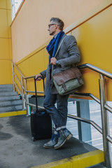 Good-looking stylish man with travel suitcase standing on stairs