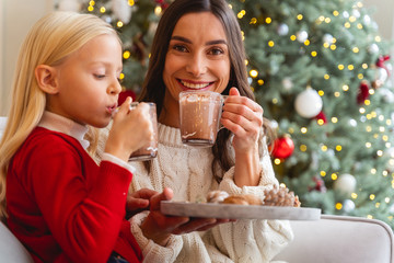 Pleased Caucasian mother and daughter drinking cocoa