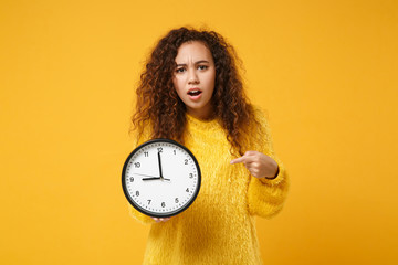 Perplexed young african american girl in fur sweater posing isolated on yellow orange wall...