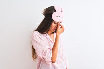 Young beautiful woman wearing sleep mask and pajama over isolated white background tired rubbing nose and eyes feeling fatigue and headache. Stress and frustration concept.