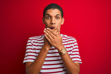 Fototapeta na wymiar Young handsome arab man wearing striped t-shirt over isolated red background shocked covering mouth with hands for mistake. Secret concept.