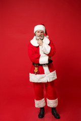 Pensive elderly gray-haired mustache bearded Santa man in Christmas hat posing isolated on red wall background, studio portrait. Happy New Year 2020 celebration holiday concept. Mock up copy space.