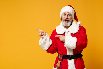 Fototapeta na wymiar Cheerful elderly gray-haired bearded mustache Santa man in Christmas hat posing isolated on yellow background. New Year 2020 celebration holiday concept. Mock up copy space. Point index fingers aside.