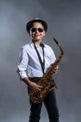 Fototapeta na wymiar Glücklicher Junge mit Altsaxophon vor grauem Hintergrund