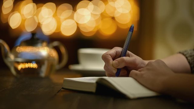 Woman keeps a diary while sitting in cozy cafe with cup of tea. Female hands writes in notebook