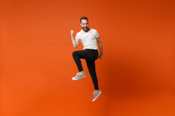 Fototapeta na wymiar Happy joyful young man in casual white t-shirt posing isolated on bright orange wall background studio portrait. People lifestyle concept. Mock up copy space. Having fun jumping, doing winner gesture.