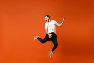 Fototapeta na wymiar Crazy young man in casual white t-shirt posing isolated on orange wall background studio portrait. People lifestyle concept. Mock up copy space. Having fun, jumping fooling around like playing guitar.