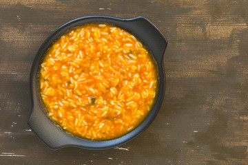 Rice in pumpkin sauce on black plate on wooden background