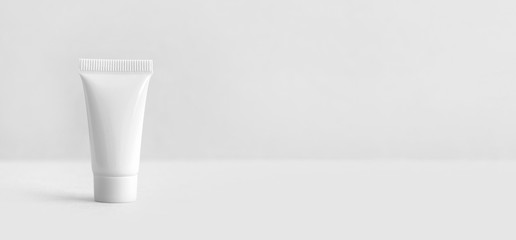 White cosmetic tube on white gray background. Minimal packages design. Blank plastic container,...