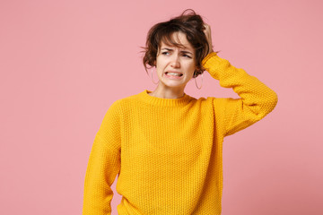 Preoccupied confused young brunette woman girl in yellow sweater posing isolated on pastel pink background in studio. People lifestyle concept. Mock up copy space. Looking aside, putting hand on head.