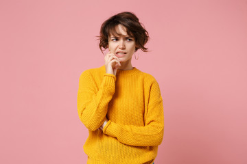 Preoccupied young brunette woman girl in yellow sweater posing isolated on pastel pink wall background in studio. People lifestyle concept. Mock up copy space. Looking aside, put hand prop up on chin.