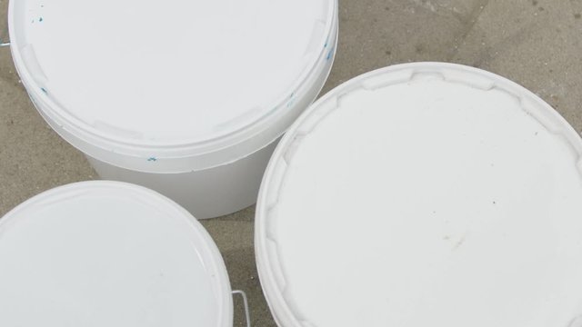hands reputting paint buckets on to the pavement. putting closed buckets down. putting on the floor. Ten liter paint cans. Painters material being put down.