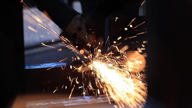 A man works circular saw, Flies of spark from hot metal, The man's hard work, Man Chlef and smooth surface, Man worked over the steel, Close-up of hand tool