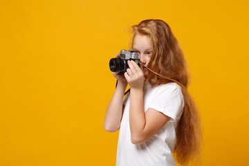 Little ginger kid girl 12-13 years old in white t-shirt isolated on yellow wall background children studio portrait. Childhood lifestyle concept. Mock up copy space. Hold retro vintage photo camera.