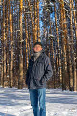 Portrait of handsome middle-aged man against beautiful winter landscape. Man walking in snowy forest in sunny frosty day. Human and nature, winter holidays, weekend at countryside concept