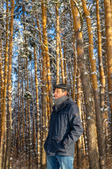 Portrait of handsome middle-aged man against beautiful winter landscape. Man walking in snowy forest in sunny frosty day. Human and nature, winter holidays, weekend at countryside concept