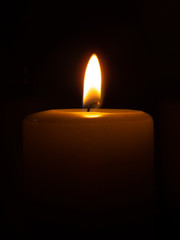 Partly visible lighted candle infront of black background