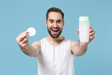 Bearded young man 20s years old in white shirt hold in hand cotton pad isolated on blue pastel wall background, studio portrait. Skin care healthcare cosmetic procedures concept. Mock up copy space.