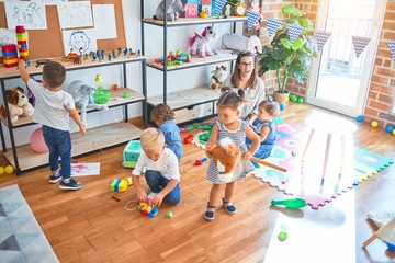 Beautiful teacher and group of toddlers playing around lots of toys at kindergarten