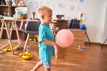 Young caucasian kid playing at kindergarten with toys. Preschooler boy happy at playroom.