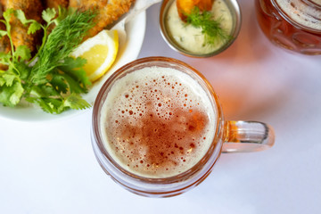 Mug with beer and beer snacks. Corn chips with sauce, fish and greens.