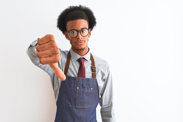 Young african american shopkeeper man wearing apron glasses over isolated white background looking unhappy and angry showing rejection and negative with thumbs down gesture. Bad expression.