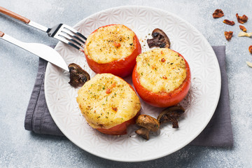 Baked whole tomatoes stuffed with mushrooms and cheese with spices on a light concrete background.