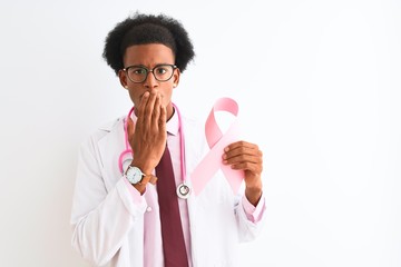 Young african american doctor man holding cancer ribbon over isolated white background cover mouth with hand shocked with shame for mistake, expression of fear, scared in silence, secret concept