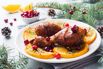 Baked chicken drumstick with oranges and cranberries in a plate light grey background. Christmas food Table with decorations.