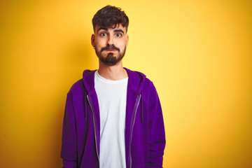 Obraz premium Young man with tattoo wearing sport purple sweatshirt over isolated yellow background puffing cheeks with funny face. Mouth inflated with air, crazy expression.