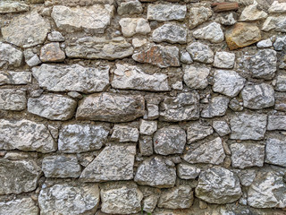 Old style retro and traditional way of building a wall with uneven stones and rocks glued with cement with sign of damage making a cool background wallpaper