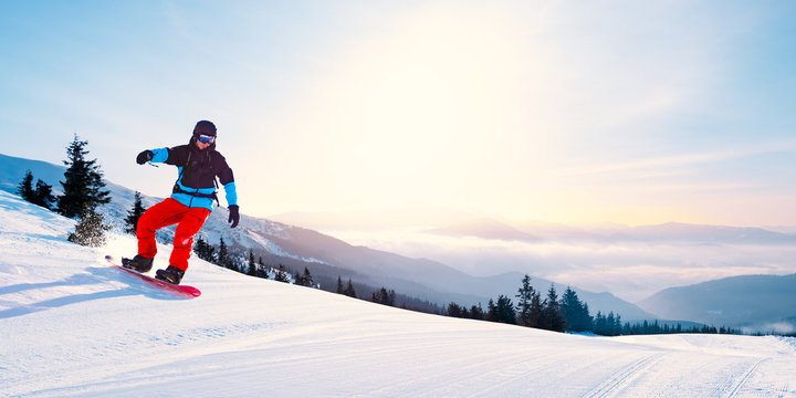 Young Snowboarder Riding Red Snowboard in Mountains at Sunny Day. Snowboarding and Winter Sports