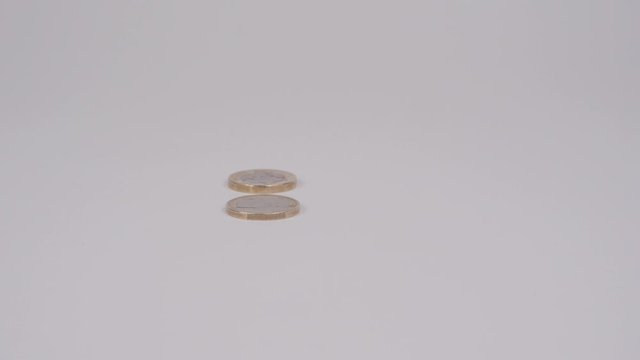 Slow motion euro and pound coins rolling in to each other, crashing and falling down 