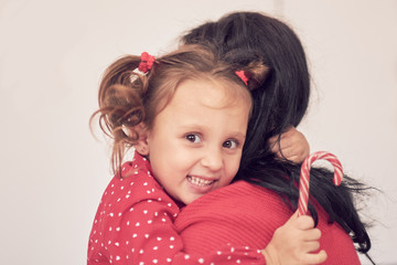 mom and daughter have fun together. a woman in a warm red knitted sweater hugs her little daughter in a red dress. family values