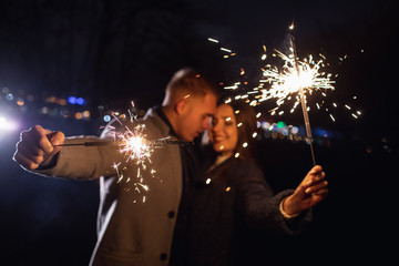 Selective focus of sparklers in hands of young couple enjoying holiday time outdoors