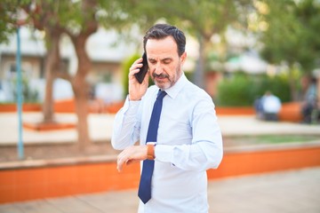 Middle age handsome businessman talking on the smartphone looking at watch smiling