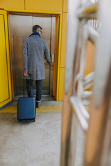 Fototapeta na wymiar Elegant man with travel suitcase pressing the elevator button