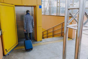 Stylish man with travel suitcase waiting for lift