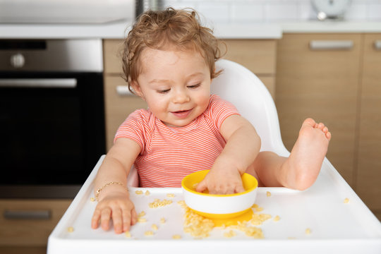 Cute Baby In High Chair Eating Pasta With Hands