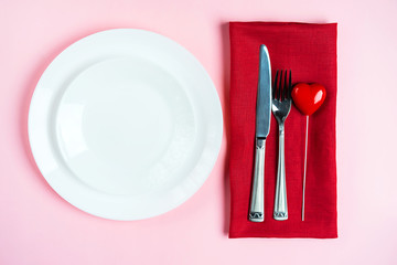 Festive table setting for Valentine's Day with fork, knife and hearts on pink table background.