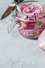 Pickled chopped red onion in vinegar in a glass jar. A delicious side dish for meat and fish dishes. Light grey background.