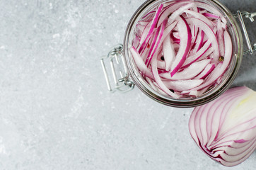 Pickled chopped red onion in vinegar in a glass jar. A delicious side dish for meat and fish dishes. Light grey background.