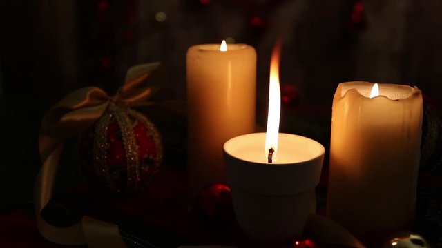 Christmas mood: three lighted candles, one with a big flame in the foreground, red and golden balls, decoupage balls, satin gold ribbon, Christmas decorations filmed in low light and bokeh effect